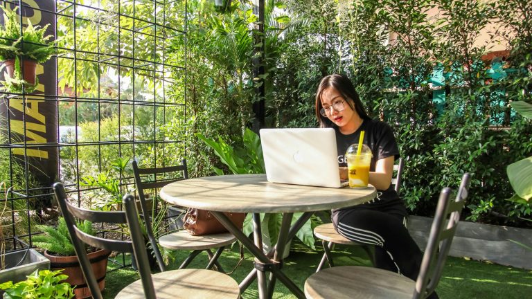 Deze afbeelding toont een vrouw die in een prachtige tuin werkt, wat de vrijheid en flexibiliteit van het leven als digital nomad symboliseert.